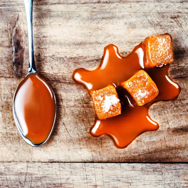 Homemade Caramel sauce flowing on caramel candies on wooden board