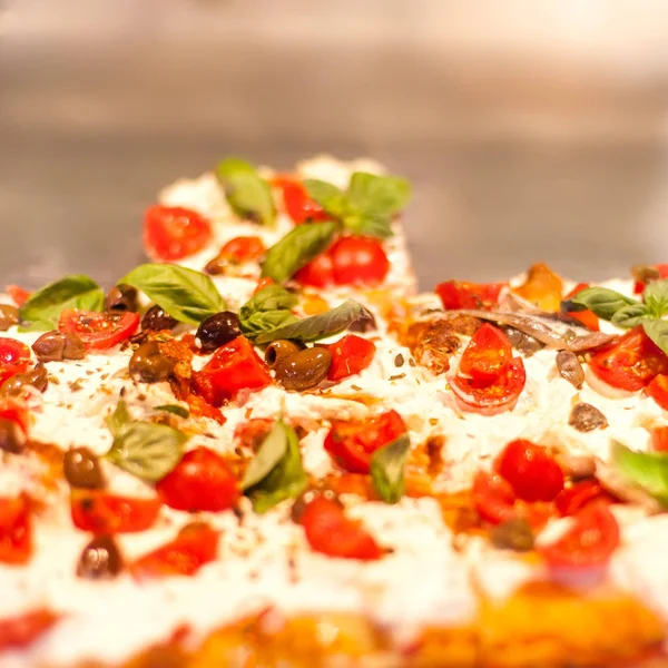 Pizza Take Away pieces on a stall in pizzeria in Italy,  Traditional Italian Focaccia with tomatoes, black olives and chees