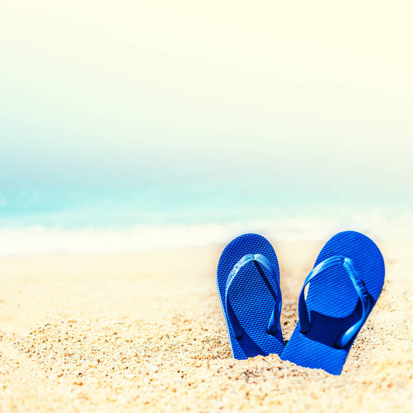 Summer holiday beach background with flip flops on a tropical beach. Slippers from a sand on a beach, funny concept