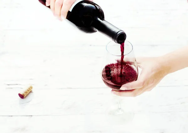 Woman hand Pouring red  wine from bottle into the wine glass on white wooden background with copyspace