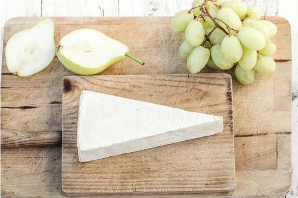 ブドウや果物 まな板の上の新鮮なブリーチーズ平面図です 白い素朴な木製の背景にブリーチーズ カマンベール チーズ — ストック写真