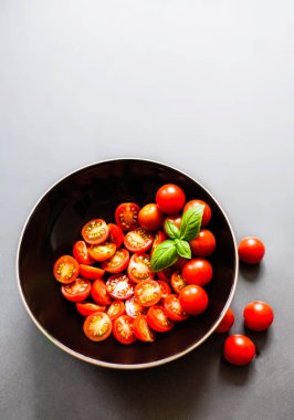 Taze kiraz domates fesleğen yaprağı üzerinde siyah koyu plaka ile boşaltmak taş kara tahta kayrak. Organik salata malzemeleri