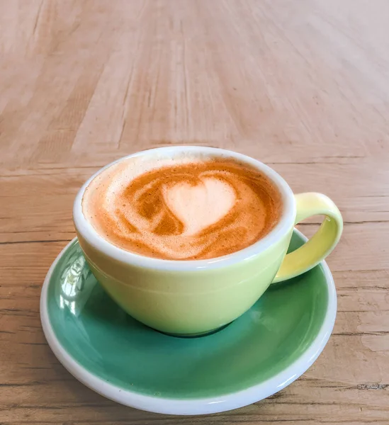 Cup of coffee with heart pattern foam  in a yellow cup on rustic wooden table background, top vie