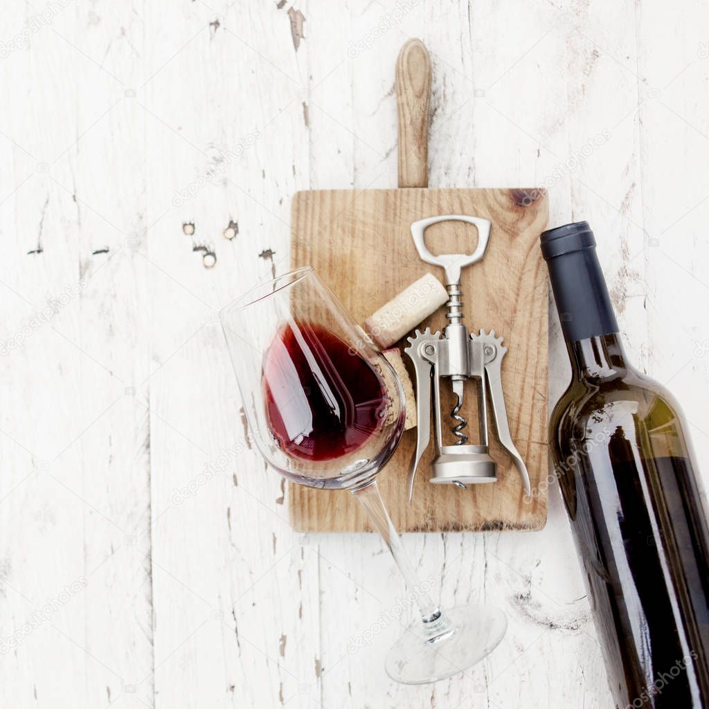 Bottle of red wine, corkscrew and wine corks on rustic white wooden background