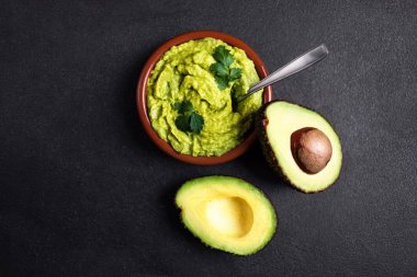 Koyu arka plan üzerinde kesme yarım avokado kil kase guacamole sos. Kopya spac ile Üstten Görünüm