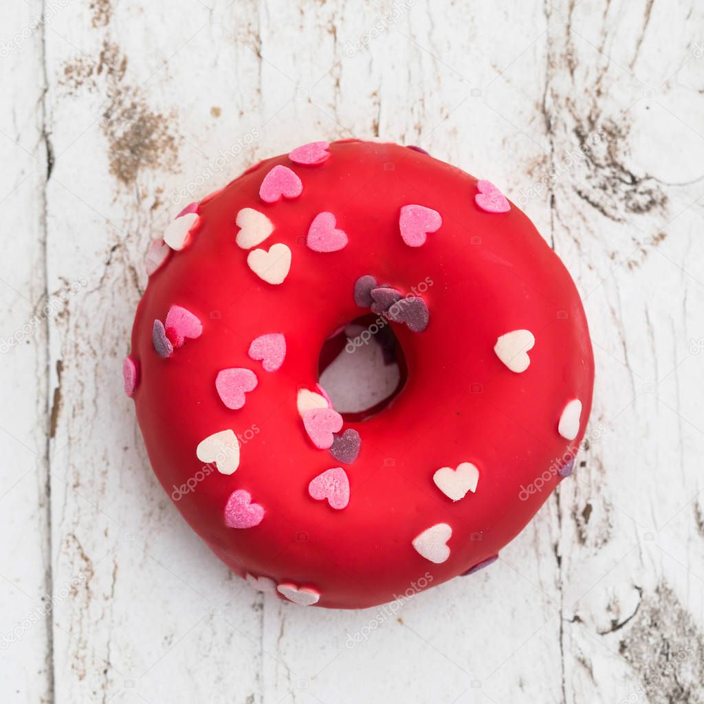 Donut with heart sprinkles on white wooden background. Donut for bakery menu. Valentine Day food  idea. Funny donu
