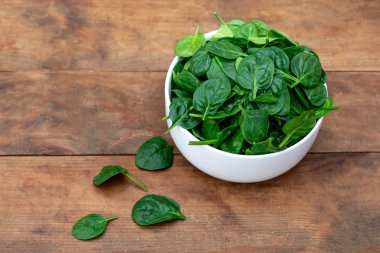 Ahşap arka plan üzerinde kase taze bebek ıspanak yaprakları