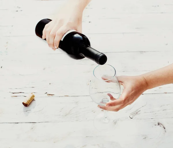 Nalévá červené víno z láhve v prázdné sklenice na víno bílé dřevo — Stock fotografie