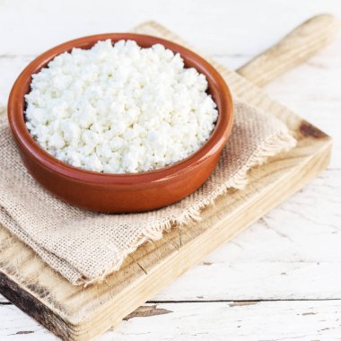 Beyaz ahşap masada seramik bir kasede ev yapımı süzme peynir. Sağlıklı yiyecekler. Taze süt ürünleri. Üst görünüm