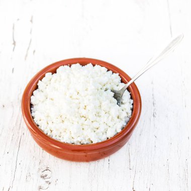 Beyaz ahşap masada seramik bir kasede ev yapımı süzme peynir. Sağlıklı yiyecekler. Taze süt ürünleri. Üst görünüm