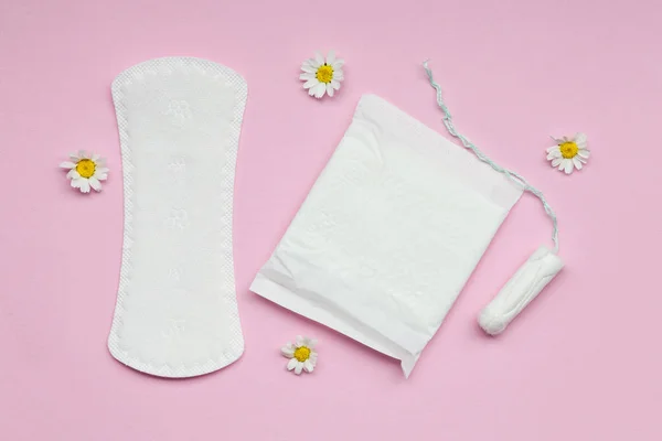 menstruation cycle, feminine hygiene and protection products, sanitary pads, tampon and chamomile flowers on pastel pink background, top view, flat layout