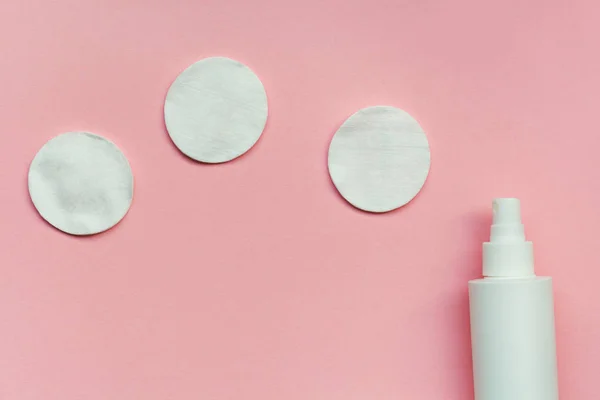 skincare routine, makeup removing, white facial cotton pads and bottle of micellar water, woman skin and body care product isolated on pastel pink background, top view, flat layout
