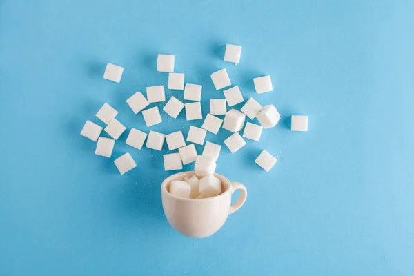 coffee cup full of sugar cubes isolated on pastel blue background, hidden sugar in sweet drinks, diabetes risk, studio shot, top view, flat lay