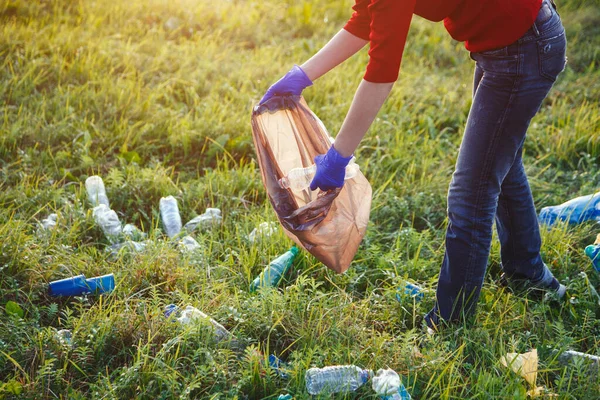 volunteer young woman collecting garbage, holding full bag of waste and plastic bag, cleanup, land pollution, environmental problem, copy space, sunset light, world environment day