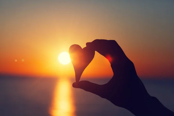 silhouette of female hand holding wooden heart,against sunset light, love and feelings concept