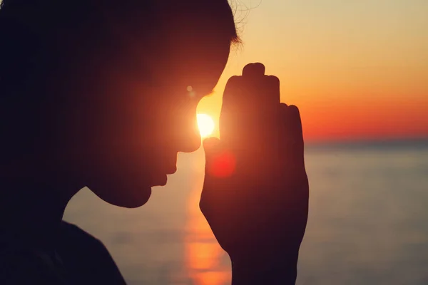 silhouette of young woman raising hands praying at sunset or sunrise light, practicing yoga on the beach, religion, freedom and spirituality concept