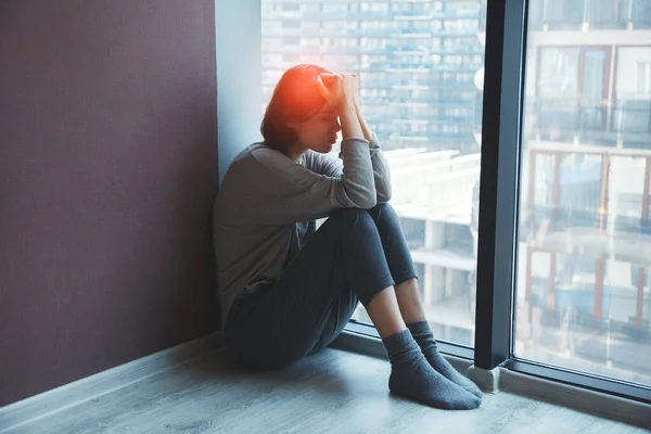 young stressed tired woman sitting on the floor at home suffering from migraine headache, having mental problems