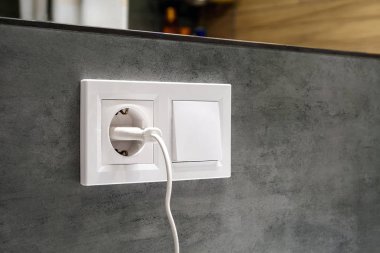Bir grup beyaz Avrupa elektrik prizinin birbirine yakın köşegen görüntüsü ve modern bir banyodaki aynanın altındaki beton gri bir duvarda bulunan bir anahtar.