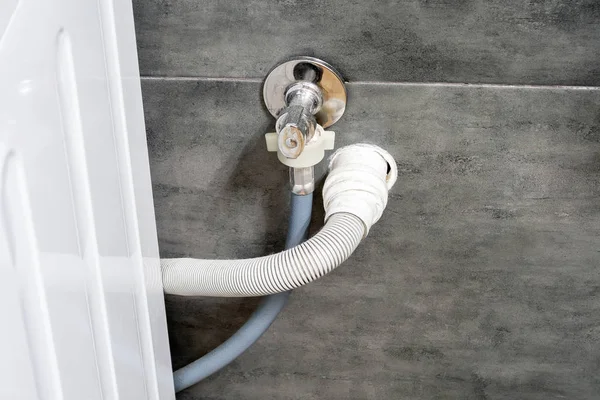 Dirty drain and water hoses for the washing machine running into a wall covered with gray concrete tile. Design options in a comfortable modern bathroom — Stock Photo, Image