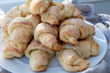 Beyaz bir tabakta gri bir bezin yanında duran kaymak hamurundan çıkan şekerli kruvasan. Fırından yeni çıkmış tatlı çörekler.