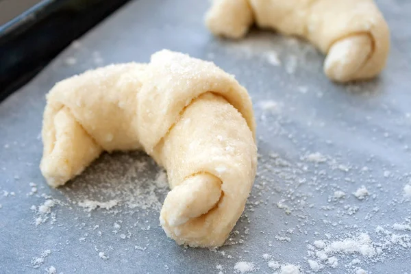 A closeup view of a croissant prepared for baking from a curd dough sprinkled with sugar lying on a parchment baking paper covered with flour — Stock Photo, Image