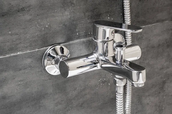 Хромированная металлическая решетка для горячей и холодной воды с душем, смонтированная в стене, облицованной плиткой, имитирующей бетон с каплями воды в современной ванной комнате — стоковое фото