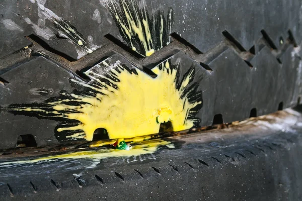 Peinture jaune éclaboussure d'un paintball écrasé sur un vieux pneu de voiture avec un motif de bande de roulement en zigzag. Concentration sélective — Photo