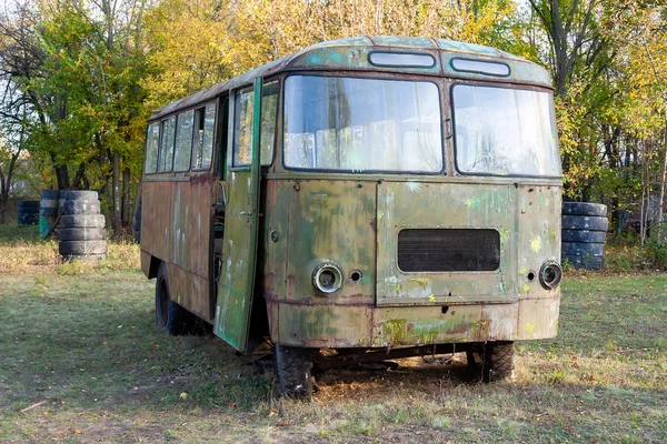 Zielony stary zardzewiały autobus ze śladami farby i przebitymi oponami stoi na leśnej polanie pośród drzew. Schronisko na placu zabaw dla paintballa taktycznego — Zdjęcie stockowe