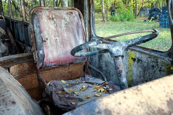 Brudne stare siedzenie kierowcy z żółtymi liśćmi i kierownicą w zardzewiałym autobusie z wybitymi szybami i śladami farby w lesie. Bunkier na placu zabaw paintballa taktycznego. Widok z bliska — Zdjęcie stockowe