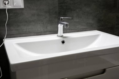 Modern beyaz dikdörtgen lavabo krom metal musluk ile sıcak ve soğuk su için şık bir banyoda gri beton duvarlı. Seçici odak