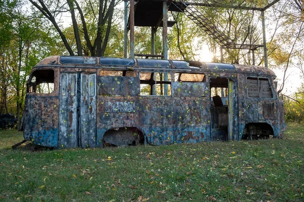 Stary zardzewiały autobus ze śladami farby i bez kół stoi w lesie obok metalowej wieży. Schronisko na placu zabaw dla paintballa taktycznego — Zdjęcie stockowe