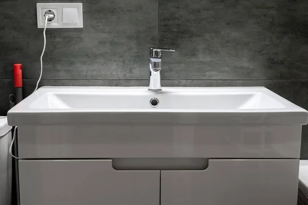 Современная белая прямоугольная раковина с хромированным металлическим краном для горячей и холодной воды в стильной ванной комнате с серой бетонной стеной. Селективный фокус — стоковое фото
