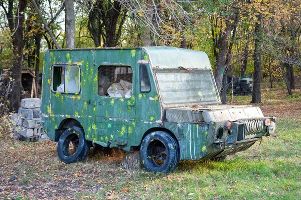 Ein altes grünes Auto mit Netzen an den Fenstern und Pappkartons drinnen, mit Farbspuren und platten Reifen steht auf einer Waldlichtung zwischen den Bäumen. Unterstand auf dem taktischen Paintball-Spielplatz — Stockfoto