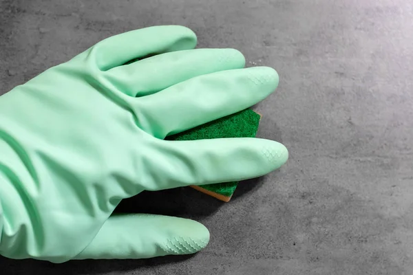 Una mano in un guanto di gomma verde menta pulisce bagnato muro di cemento piastrelle grigie con una spugna arancione. Pulizia in un bagno moderno. Focus selettivo — Foto Stock