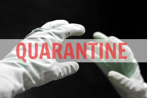 A hand in a mint green rubber glove reaches for its reflection in the mirror in the dark black room. In the center of the photo is a white transparent stripe with a red inscription: quarantine — 스톡 사진