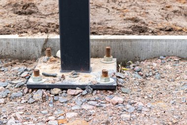 Beton kaldırım kenarına çakıllarla kaplı bir inşaat sahasında dört çapa bulunan bir reklam panosu ya da ışıklandırma sütununun kurulumu