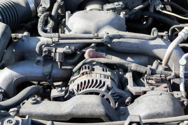 Açık kaputun altındaki dört silindirli motor kompartımanının tozlu detayları. Alternatör ve emme manifoldu. Güneşli bir günde kapanış görüntüsü