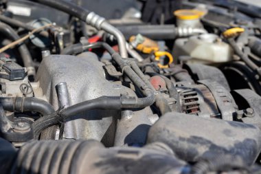 Açık kaputun altındaki dört silindirli motor kompartımanının tozlu detayları. Alternatör ve emme manifoldu. Güneşli bir günde yakın bir bakış açısı. Seçici odak