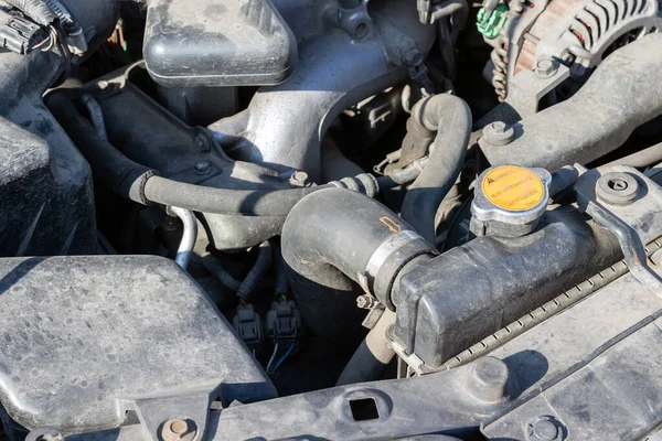 Açık kaputun altındaki dört silindirli motor kompartımanının tozlu detayları. Radyatör kapağı ve hortum. Güneşli bir günde kapanış görüntüsü