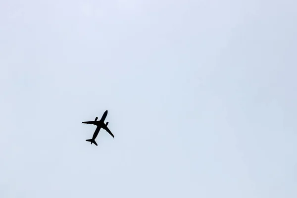 Black silhouette of a flying airplane against a blue gray sky background