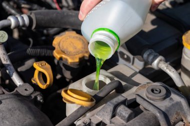 Genişleme tankına antifriz döken bir el. Açık kaputun altındaki dört silindirli motor kompartımanının tozlu detayları. Güneşli bir günde kapanış görüntüsü