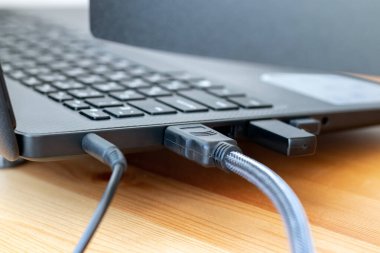 Güç ve hdmi kabloları, ve kablosuz dongle USB fare alıcısı gri bir dizüstü bilgisayarın yan tarafında ahşap bir masada. Seçici odaklanma. Yakın görünüm