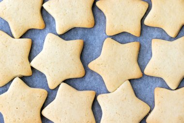 Fırından yeni çıkmış parşömen kağıdıyla fırında pişmiş kurabiye ve yıldız şeklinde kurabiyeler. Kahvaltıda atıştırmalık çay. Seçici odaklanma. Yakın görünüm