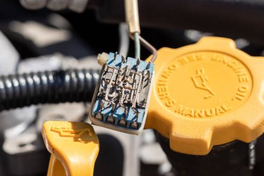 Bir petrol sondasının üzerindeki tozlu, küçük elektronik bileşen ve bir arabanın kaputunun altındaki yağ kapağı. Güneşli bir günde kapanış görüntüsü