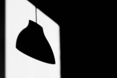 Tavan lambasının gölgesi, duvardaki güneş ışığının dikdörtgen şeklinde izi üzerinde. Siyah beyaz fotoğraf