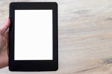 Bulanık ahşap zemin zeminine karşı insan elinde beyaz boş bir ekranı olan modern siyah elektronik bir kitap. Kopyalama alanı ile kapatma tableti