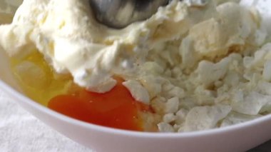 Süzme peynir, tereyağı, yumurta ve şeker beyaz kasede. Malzemeler el blenderiyle karıştırılıyor. Ekmek ya da kruvasan yapma süreci