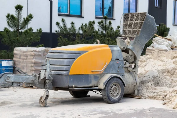 Modern beton pompa bir inşaat sahasının yanında kum yığını, çimento torbaları, bir bina ve çam ağaçları