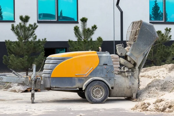Modern beton pompa bir inşaat sahasında bir kum yığını, bir bina ve çam ağaçlarının yanında