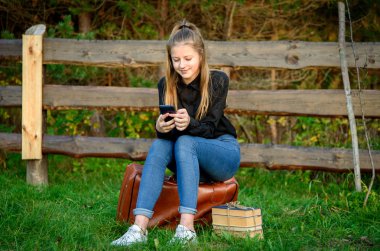 Doğada bir bavulun üzerinde oturan genç bir kız bekliyor..